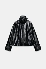 Chaqueta de efecto piel en color negro con cuello subido y bufanda desmontable integrada mediante botones. Presenta manga larga con trabillas ajustables en los puños, cierre frontal con cremallera y bolsillos laterales ocultos en las costuras. El diseño incluye un bajo con elástico en la espalda y forro interior.