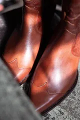 Botas estilo cowboy de cuero color marrón, con diseño de costuras decorativas en la caña y puntera estilizada. Cuentan con taco cuadrado de madera y tiradores laterales.