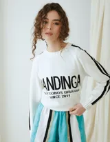 Buzo de punto blanco con rayas negras en las mangas y la inscripción "MANDINGA" y texto complementario en el pecho.