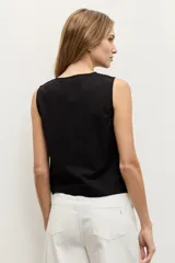 Blusa negra sin mangas, con cuello redondo y cierre frontal de botones ocultos. Presenta un aplique bordado con diseño abstracto en el lateral inferior.