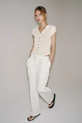 Camiseta de canalé color blanco, de corte slim fit, cuello redondo, manga corta y cierre frontal con hilera de botones oscuros a contraste.