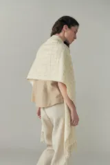 Chal de lana fina sin teñir con diseño de cuadros sutiles, cierre frontal con alamar y bolsillos de cuero metalizado. Presenta terminaciones con flecos en el ruedo y un calce estructurado en los hombros.