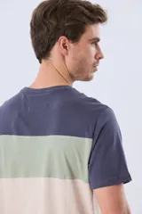 Remera de manga corta con diseño de bloques de color en tonos gris, blanco y azul marino. Cuenta con cuello redondo y una estampa tipográfica en el centro del pecho.
