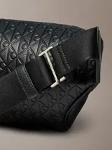 Riñonera Calvin Klein de poliuretano color negro, con diseño de monograma grabado en relieve, cierre superior de cremallera, bolsillo frontal con cremallera y correa ajustable.