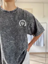 Remera gris con efecto lavado y estampado de trébol con texto en el frente. Corte holgado y mangas cortas.