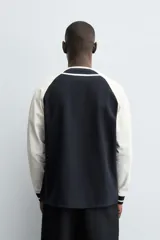 Chaqueta de corte relajado con diseño color block, cuerpo en color azul marino y mangas en color blanco. Presenta cuello redondo, cierre frontal con botones y puños de rib a rayas.
