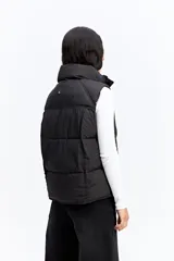 Chaleco puffer negro con cuello alto, cierre frontal y broches a presión. Diseño acolchado liviano con bolsillos laterales.