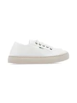 Zapatilla de lona blanca con suela de goma en tono beige. Presenta un diseño minimalista con cordones al tono y detalle de etiqueta pequeña en el lateral.