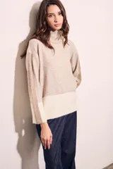 Sweater de punto con cuello alto, corte holgado y diseño color block en tonos beige y blanco.