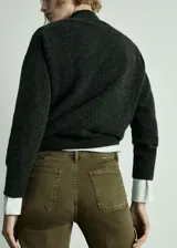 Pantalón tipo jeans de tiro medio en color verde oliva, con diseño acampanado y bajo deshilachado. Presenta dos bolsillos de parche en la parte delantera, cierre de cremallera y botón, y trabillas para cinturón.
