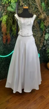 Vestido de fiesta blanco de dos piezas, con top tipo corset con ballenas y bordado de canutillos blancos y plateados, y falda larga de satén con vuelo.