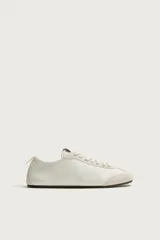 Zapatillas de cuero color blanco roto, de diseño minimalista con cordones, suela fina de goma marrón y detalles de gamuza en la puntera y los ojales.