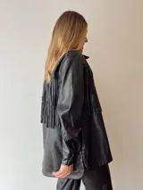 Sobrecamisa oversize de ecocuero negro con flecos en la espalda y tachas plateadas.