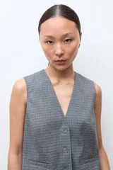 Chaleco sastrero de corte entallado con escote en V, cierre frontal con botones y bolsillos laterales simulados. Presenta un estampado de microcuadros en tonos grises.