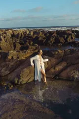 Vestido largo blanco con escote en V profundo y mangas largas acampanadas. Presenta aberturas en la parte delantera y detalles de cordones cruzados en el escote.