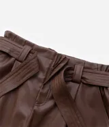 Short de cuero sintético color marrón, de tiro alto, con trabillas en la cintura, pliegues delanteros, bolsillos tipo cuchillo y cinturón para lazo.
