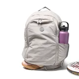 Mochila deportiva color gris, confeccionada en material textil con acabado arrugado. Presenta compartimento principal con cierre doble, bolsillo frontal con logo circular, compartimento inferior independiente para calzado y bolsillos laterales. Incluye tirantes ergonómicos ajustables y espaldera acolchada con malla transpirable.