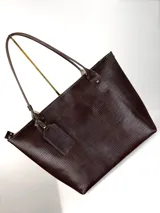 Cartera tipo tote de cuero genuino color marrón oscuro con textura de reptil. Cuenta con doble asa de hombro, cierre superior y un dije colgante de cuero a tono.