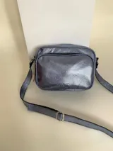 Bandolera rectangular de cuero azul metalizado con correa larga regulable. Cuenta con un bolsillo frontal con fuelle y un bolsillo trasero con cierre.