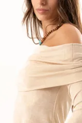 Blusa beige con hombros descubiertos, confeccionada en tela elástica con destellos de lurex. Presenta mangas largas con terminación acampanada y diseño ajustado al cuerpo.