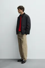 Parka de corte relajado en color negro, confeccionada en tejido de algodón con interior ligeramente acolchado. Presenta cuello de solapa en pana, cierre frontal con cremallera y bolsillos delanteros tipo plastrón con solapa y botones a presión.