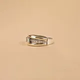 Anillo de diseño ancho compuesto por una banda central de oro pulido flanqueada por dos bandas laterales de plata con textura arenada. El segundo anillo es una alianza de plata y oro con una hilera central de circonias engastadas.