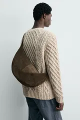 Bolso de hombro de piel con acabado serraje, color gris oscuro, con forma curva o de media luna. Presenta costuras visibles en el centro y un asa fina para llevar al hombro.