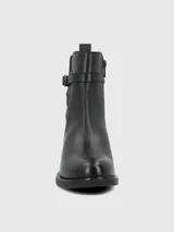 Bota corta de cuero negro con punta redonda, cierre lateral y detalle de tira con hebilla metálica en el tobillo.