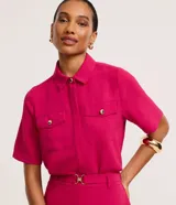 Camisa fucsia de tejido airflow texturizado, con cuello camisero, manga corta, bolsillos frontales con solapa y cierre de botones metalizados dorados.