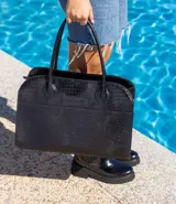 Bolso tipo tote de cuero negro con textura tipo piel de cocodrilo, doble asa de mano y cierre superior con cremallera.
