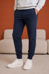 Pantalón de felpa azul marino con corte ajustado, cintura elástica con cordón de ajuste y puños acanalados en los tobillos. Cuenta con bolsillos laterales con cierre.