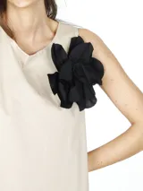 Vestido midi de poplín bicolor, beige en la parte superior y negro en la falda, con diseño irregular y flor negra decorativa en el hombro.