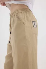 Pantalón de lino color beige, de silueta relajada, tiro medio-alto, cintura elastizada con cordón ajustable, bolsillos laterales y bolsillos traseros.