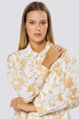 Blusa de manga larga con cuello camisero y cierre frontal de botones. Presenta un diseño estampado en tonos beige y blanco.