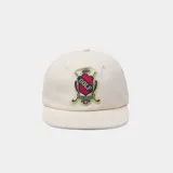 Gorra color beige con visera plana y parche bordado en el frente con escudo y la inscripción 'GOLF'.