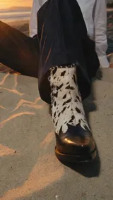 Bota corta de cuero vacuno color negro, con diseño de estilo western, punta fina y taco cuadrado de madera. Presenta costuras decorativas en la puntera y cierre lateral.