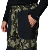 Pantalón técnico de esquí con tecnología impermeable y transpirable Omni-Tech. Presenta un diseño estampado de camuflaje en tonos verdes y negros, con paneles sólidos en negro. Incluye rodillas articuladas, ventilación en las piernas, cintura ajustable, bolsillos con cremallera y cremalleras en los puños para facilitar el uso con botas de nieve.