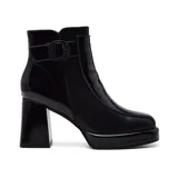 Botín de charol negro con plataforma y tacón cuadrado. Presenta una hebilla decorativa en el lateral exterior.
