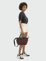 Cartera de mano modelo Le Pliage Energy en tamaño pequeño, confeccionada en lona resistente color marrón con detalles en cuero negro. Cuenta con doble asa corta, cierre principal con solapa y botón a presión, y correa larga extraíble para usar cruzada.