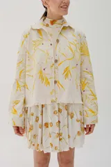 Chaqueta sobrecamisa color crema con estampado de hojas amarillas, cuello camisero, bolsillos plaqué y cierre frontal con botones.