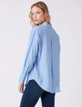 Camisa de algodón con estampado de rayas verticales finas en color azul claro. Tiene cuello con solapa, escote en V y cierre frontal con botones.