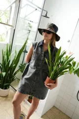 Vestido corto de jean color gris oscuro con efecto acid wash, sin mangas, con cuello camisero y cierre frontal de botones. Incluye dos bolsillos en el pecho con solapa y pespuntes decorativos.