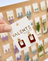 Aros colgantes de diseño geométrico, formados por un aplique superior dorado rectangular y un aro inferior rectangular esmaltado en color bordó con bordes dorados.
