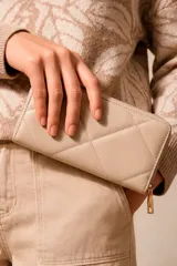 Billetera grande de cuero sintético en color beige, con diseño acolchado de costuras en rombos y cierre perimetral con tirador metálico dorado.