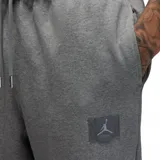 Pantalón de jogging Nike Jordan, confeccionado en tejido fleece gris melange. Presenta cintura elástica con cordón ajustable, bolsillos laterales y puños elásticos en los tobillos. Incluye un pequeño parche con el logo Jumpman en la pierna izquierda.