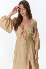 Vestido color beige de lino, con escote en V, mangas largas abullonadas y lazos frontales. Tiene corte a la cintura y falda larga con tajo frontal.