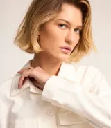 Campera corta color blanco hueso, estilo trucker, con cuello clásico, cierre abotonado, bolsillos cargo con solapa en el pecho y mangas largas con puños abotonados.