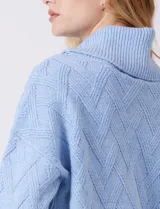 Buzo de punto grueso con textura en relieve, de cuello volcado y mangas largas con hombros caídos. Presenta puños y ruedo con terminación en rib.