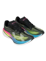 Championes de running Under Armour Velociti Elite 3, diseñados para carreras de larga distancia. Presentan una parte superior de tejido elástico en tonos oscuros con detalles en amarillo neón y blanco. La entresuela destaca por su diseño multicolor con capas en rosa, amarillo y azul, sobre una base blanca, incorporando placa de fibra de carbono para mayor retorno de energía.