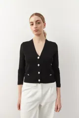 Cárdigan negro corto de tejido de punto, con escote en V, corte ajustado, cierre frontal con botones dorados texturizados y bolsillos simulados con botones dorados.